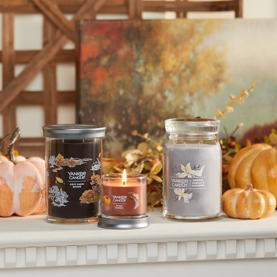 cozy cabin escape signature large tumbler candle, spiced pumpkin signature small tumbler candle, and smoked vanilla and cashmere signature large jar candle on mantle