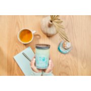 inspire scent of the year signature large tumbler candle being held above wooden table image number 5