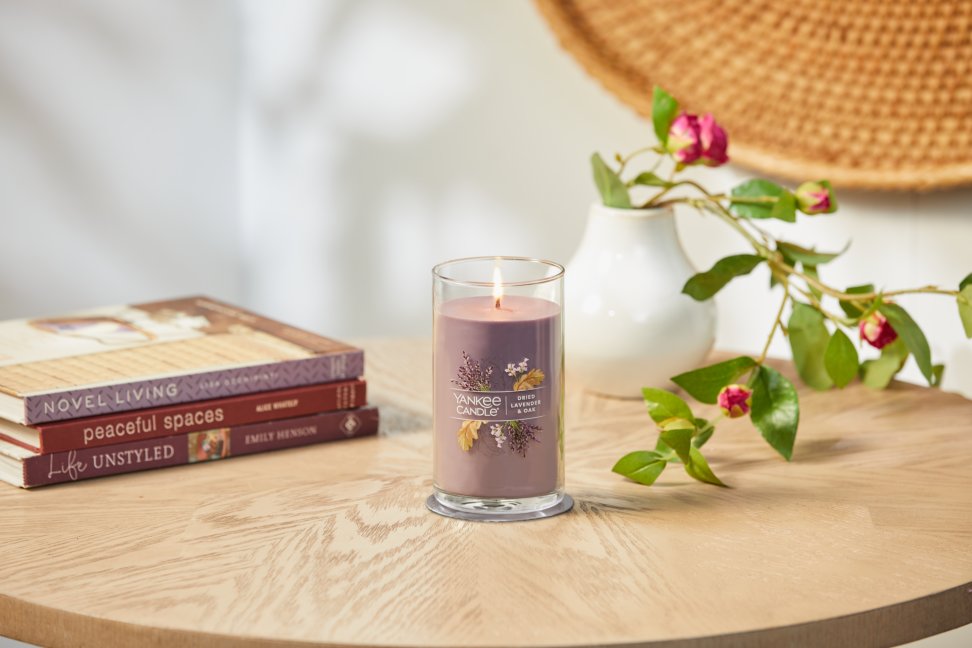 lit dried lavender and oak signature medium pillar candle on wooden table next to books and a flower vase
