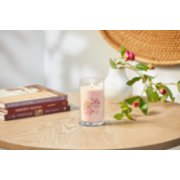 lit pink cherry and vanilla signature medium pillar candle on wooden table next to books and a flower vase image number 4