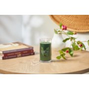 lit balsam and cedar signature medium pillar candle on wooden table next to books and a flower vase image number 4