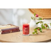 lit sparkling cinnamon signature medium pillar candle on wooden table next to books and roses image number 4