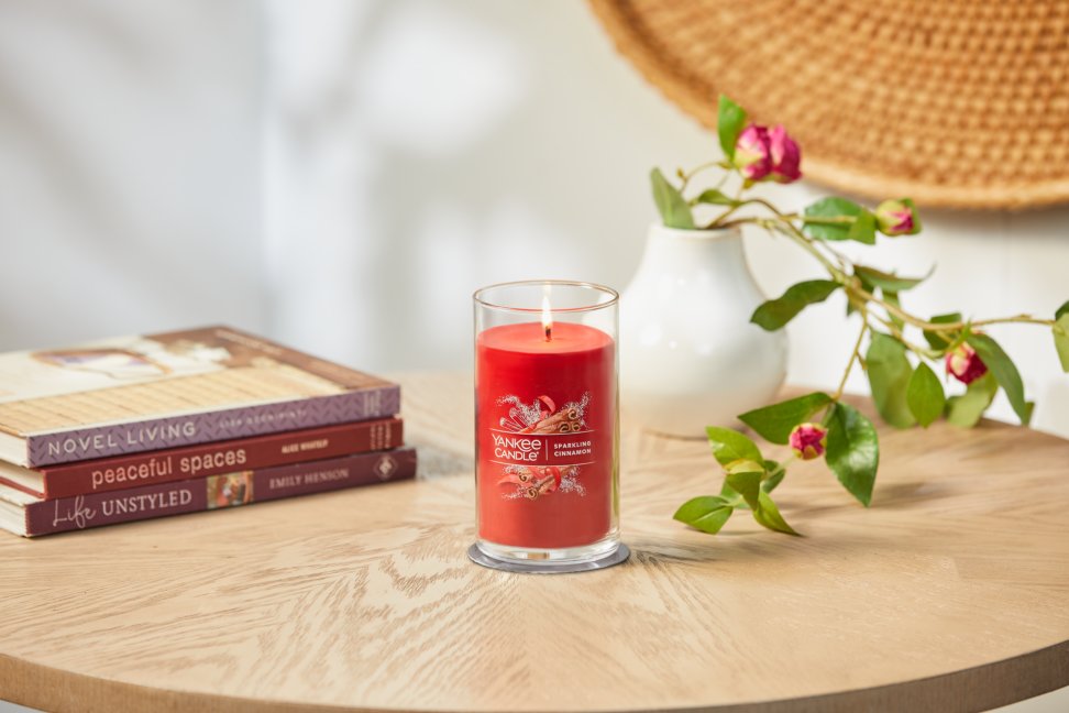 lit sparkling cinnamon signature medium pillar candle on wooden table next to books and roses