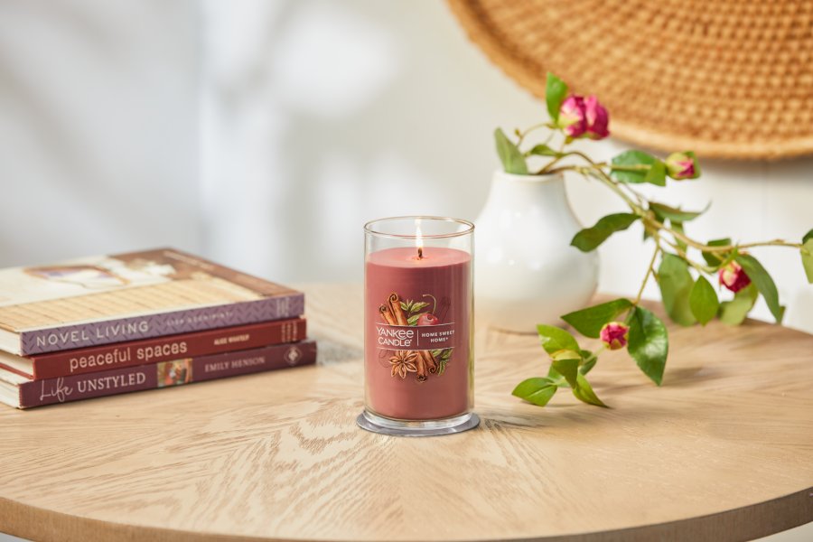 lit home sweet home signature medium pillar candle on wooden table next to books and roses