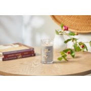 lit smoked vanilla and cashmere signature medium pillar candle on wooden table next to books and a flower vase image number 4
