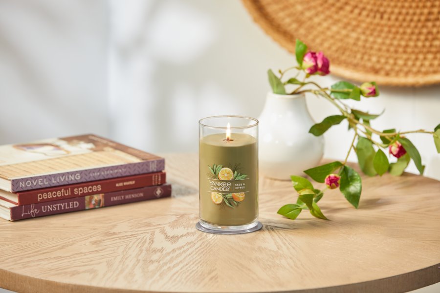 lit sage and citrus signature medium pillar candle on wooden table next to books and a flower vase