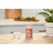 lit sugared cinnamon apple signature medium pillar candle on wooden counter next to a potted plant image number 4