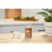 lit pumpkin banana scone signature medium pillar candle on wooden counter next to a potted plant image number 4