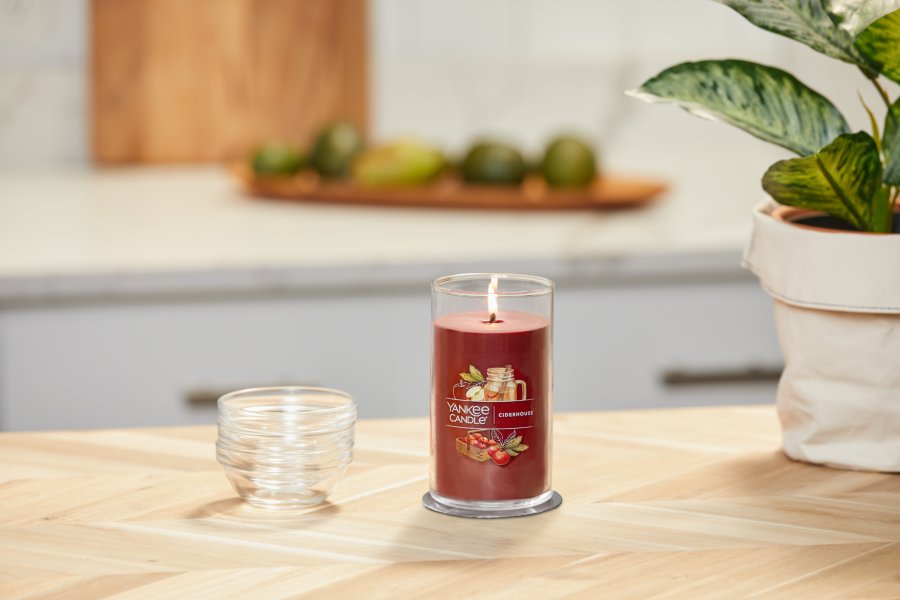 lit ciderhouse signature medium pillar candle on wooden counter next to a potted plant