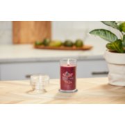 lit cranberry chutney signature medium pillar candle on wooden counter next to a potted plant image number 4