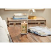 lit sun and sand signature medium pillar candle on wooden table next to a book image number 4