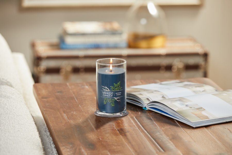 lit bayside cedar signature medium pillar candle on wooden table next to a book