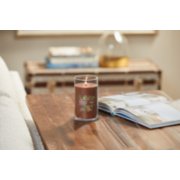 lit praline and birch signature medium pillar candle on wooden table next to a book image number 4