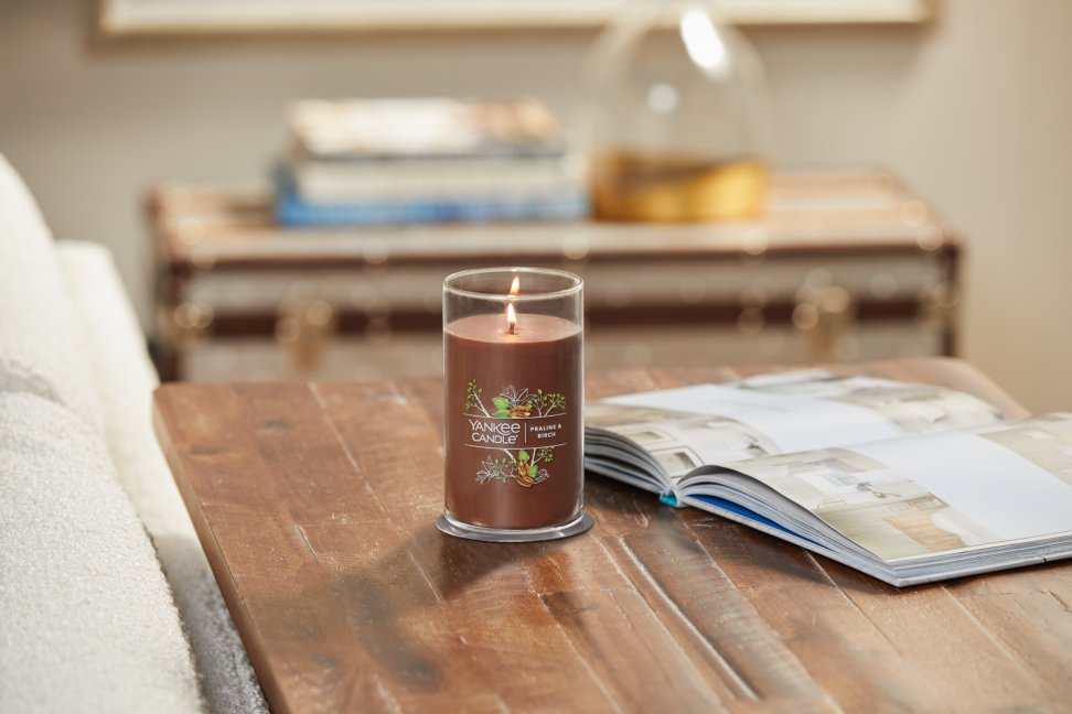 lit praline and birch signature medium pillar candle on wooden table next to a book
