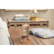 lit amber and sandalwood signature medium pillar candle on wooden table next to open book image number 4