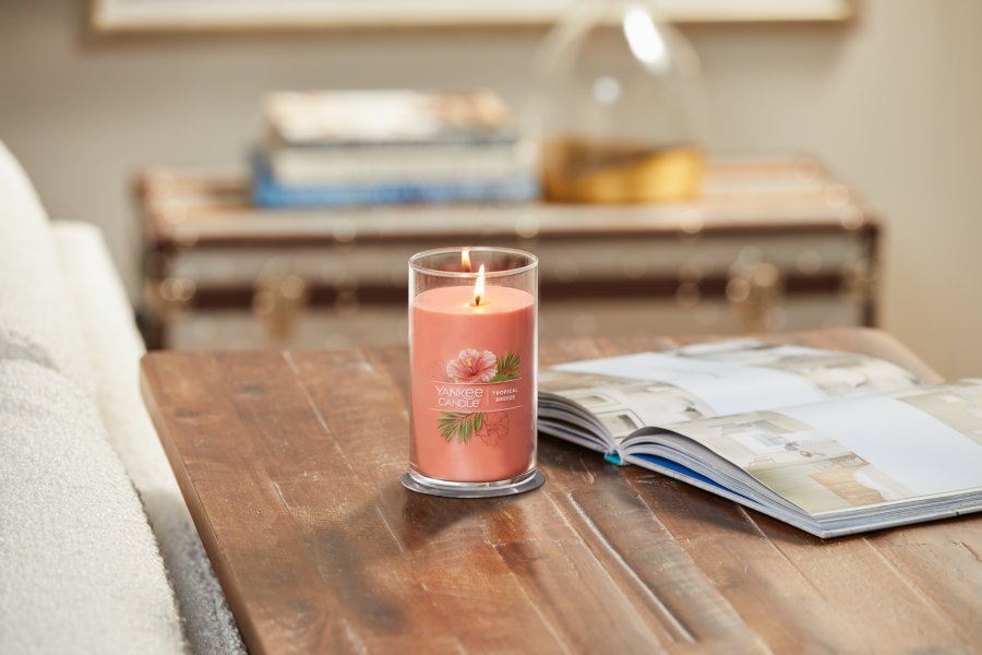 lit tropical breeze signature medium pillar candle on wooden table next to open book