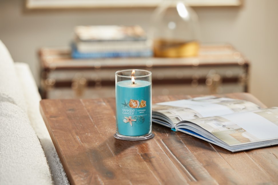 lit catching rays signature medium pillar candle on wooden table next to open book