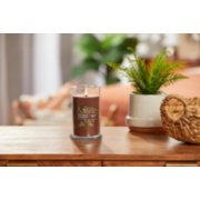 lit praline and birch signature medium pillar candle on wooden table next to a potted plant and basket image number 3