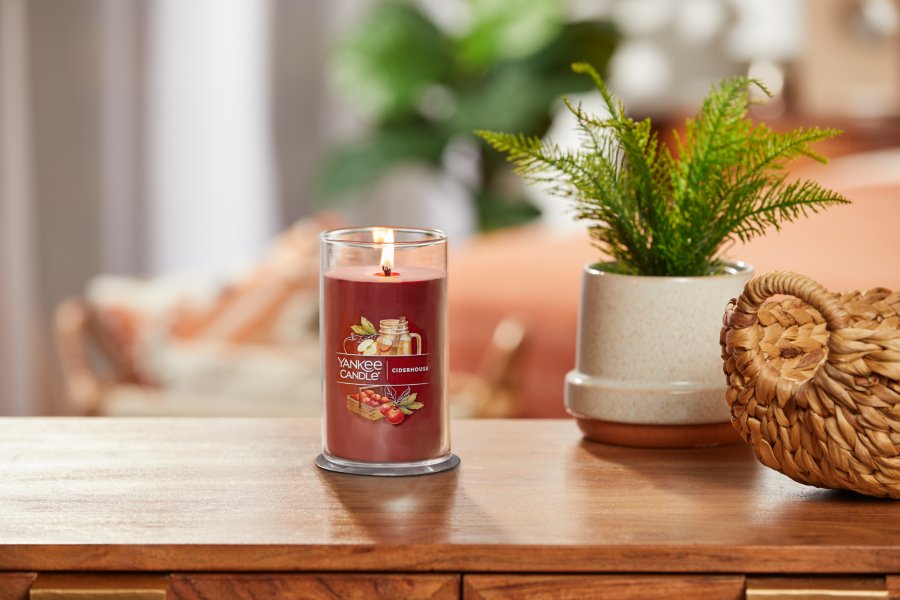 lit ciderhouse signature medium pillar candle on wooden table next to a potted plant and basket