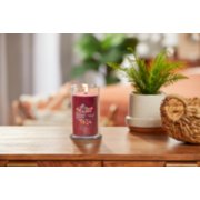lit cranberry chutney signature medium pillar candle on wooden table next to a potted plant and basket image number 3