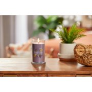 lit dried lavender and oak signature medium pillar candle on wooden table next to a potted plant and basket image number 3
