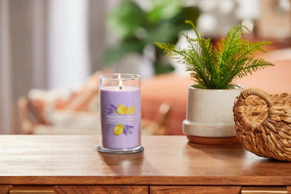 lit lemon lavender signature medium pillar candle on wooden table next to a potted plant and basket