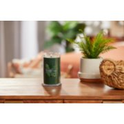 lit balsam and cedar signature medium pillar candle on wooden table next to a potted plant and basket image number 3