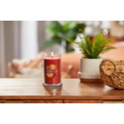 lit kitchen spice signature medium pillar candle on wooden table next to a potted plant and basket image number 3