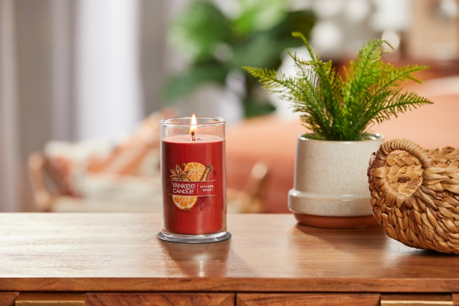 lit kitchen spice signature medium pillar candle on wooden table next to a potted plant and basket