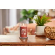 lit sugared cinnamon apple signature medium pillar candle on wooden table next to a potted plant and basket image number 3
