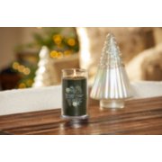 lit silver sage and pine signature medium pillar candle on wooden table next to a white and silver glitter tree image number 4