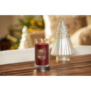 lit holiday zest signature medium pillar candle on wooden table next to a white and silver glitter tree image number 4