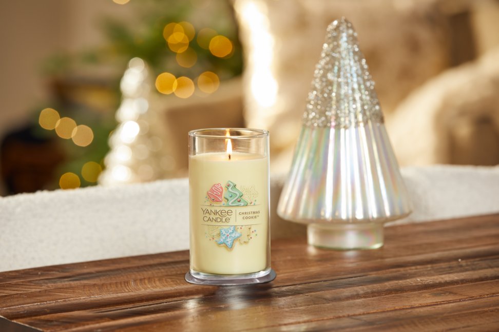 lit christmas cookie signature medium pillar candle on wooden table next to a white and silver glitter tree