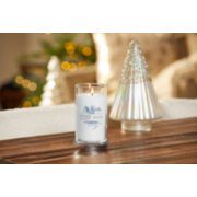 lit snow globe wonderland signature medium pillar candle on wooden table next to a white and silver glitter tree image number 4
