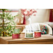 the holiday knits collection mistletoe 3 wick candle, red apple wreath 3 wick candle, balsam and cedar 3 wick candle, and sparkling cinnamon 3 wick candle on a wood table in a living room setting image number 3