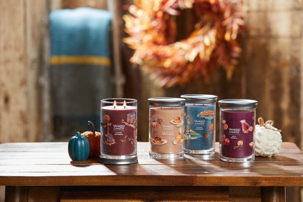 the daydreaming of autumn collection featuring autumn daydream signature large tumbler candle, pumpkin maple creme caramel signature large tumbler candle, evening riverwalk signature large tumbler candle, spicy sangria signature large tumbler candle on a wood table with white, blue, and orange decorative pumpkins