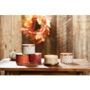 the autumn stitch collection featuring macintosh 3 wick candle, autumn wreath 3 wick candle, apple pumpkin 3 wick candle, pumpkin banana scone 3 wick candle, and spiced pumpkin 3 wick candle on a wood table next to a white decorative pumpkin image number 3