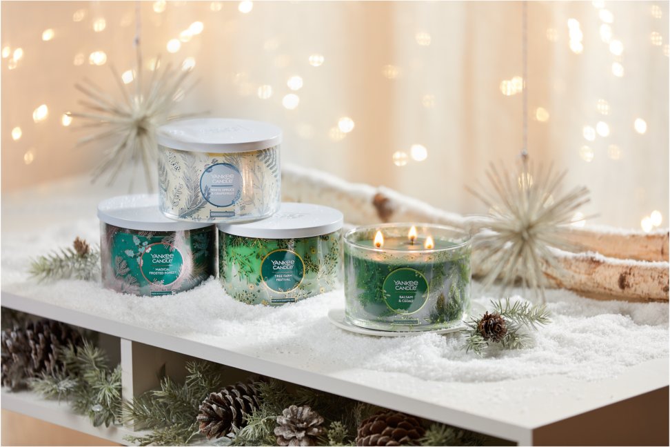 four festive three wick candle on snowy surface with pine cones birch branches and evergreens