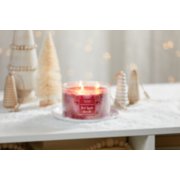 red apple wreath three wick candle on white plate on snowy surface with rustic wood and brush christmas trees image number 3