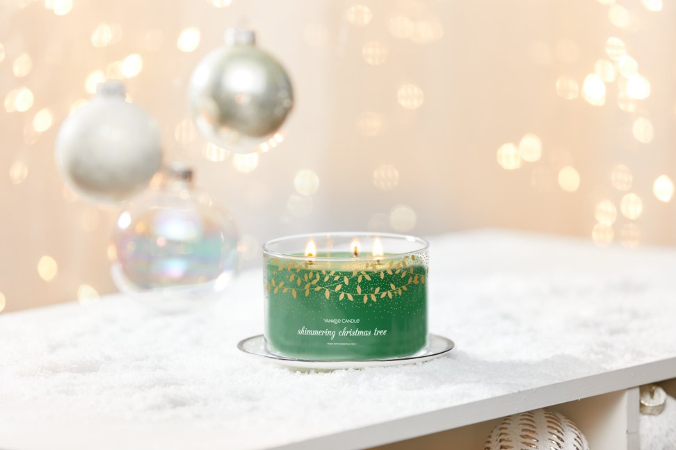 shimmering christmas tree three wick candle on plate on snowy surface with white ornaments and gold sparkles
