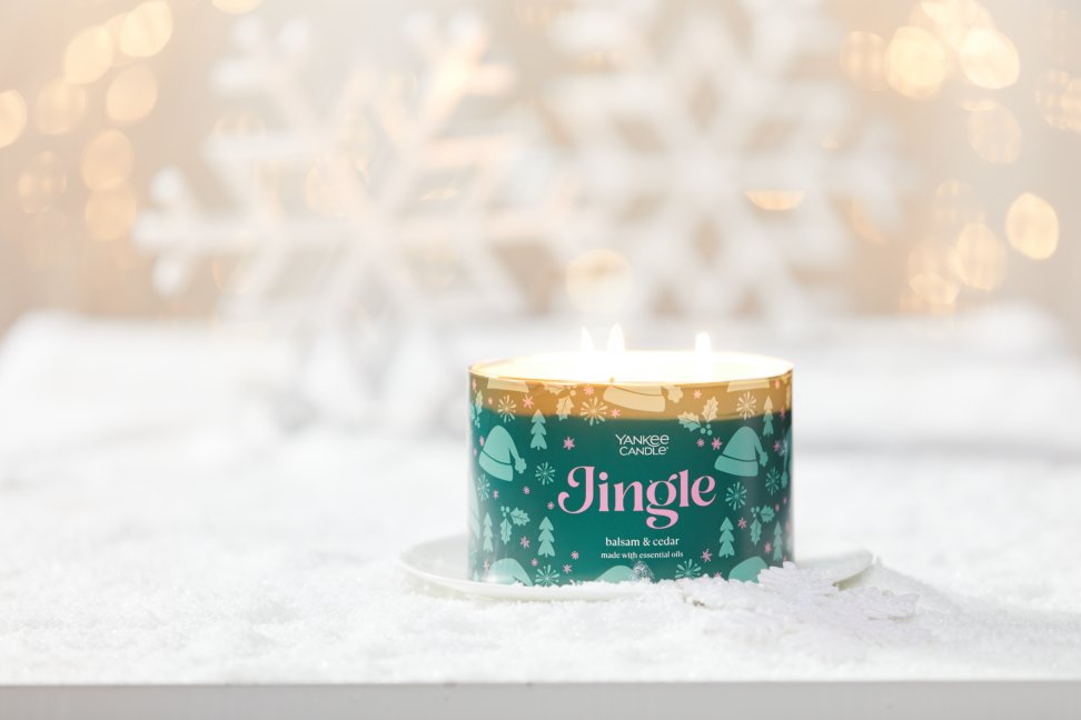 jingle three wick candle on plate on snowy surface with large snowflakes and gold sparkles