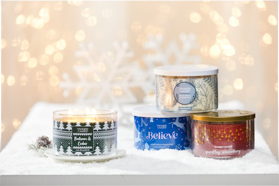 four three wick candles on snowy surface with large snowflakes and gold sparkles