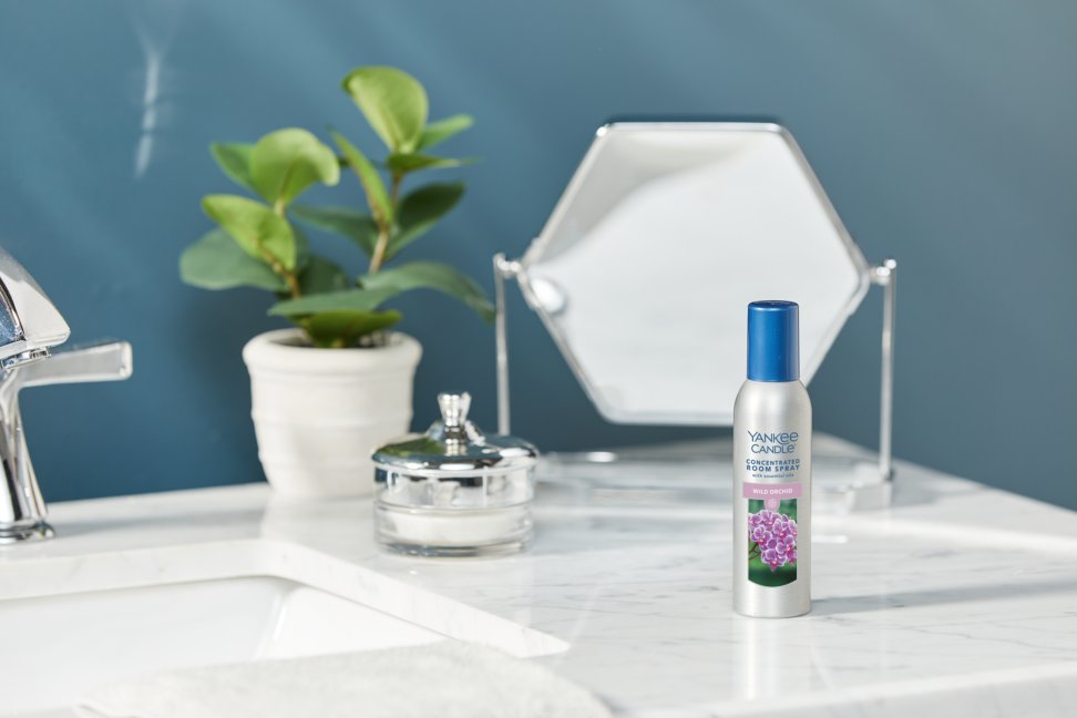 wild orchid concentrated room spray on a marble countertop next to a silver container, a plant, and a mirror