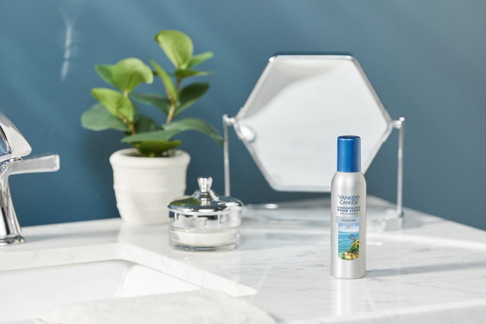ocean air concentrated room spray on a marble countertop next to a silver container, a plant, and a mirror