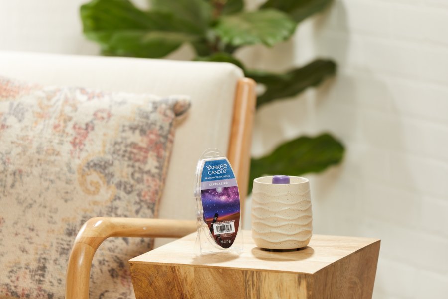 a sandstone electric wax melt warmer and stargazing wax melts on a wood side table next to a white chair with a patterned decorative pillow