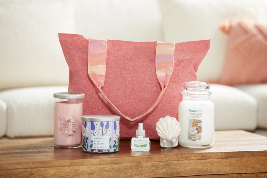 the Spring Fragrance Tote featuring a Pink Sands™ Signature Medium Pillar Candle, a Lilac Blossoms 3-Wick Candle, a Clean Cotton® ScentPlug® Refill, a Seashell ScentPlug® Diffuser, and a Coconut Beach Original Large Jar Candle on a table