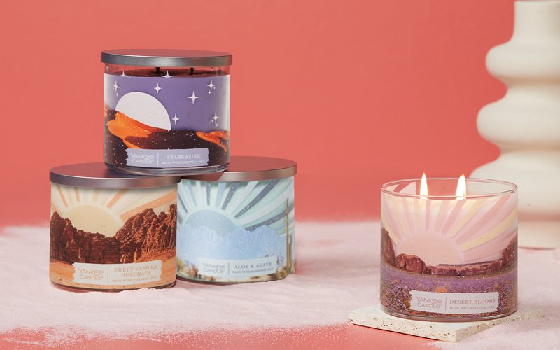 a stargazing 3-Wick candle, a sweet vanilla horchata 3-Wick candle, an aloe & agave 3-Wick candle, and a desert blooms 3-Wick candle on a table with sand
