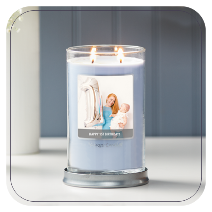 a blue-colored signature large tumbler candle with a personalized photo label with a woman and baby and happy 1st birthday messaging on a table