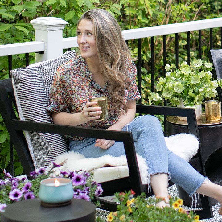 woman on outdoor porch with medium outdoor candle in foreground