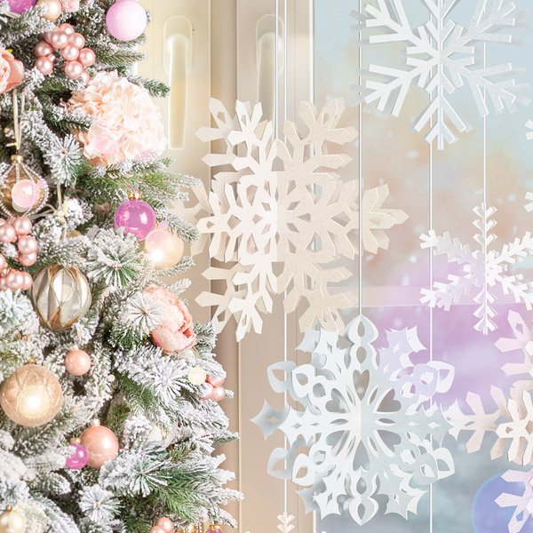 a frosted and decorated tree next to snowflakes hanging by a window